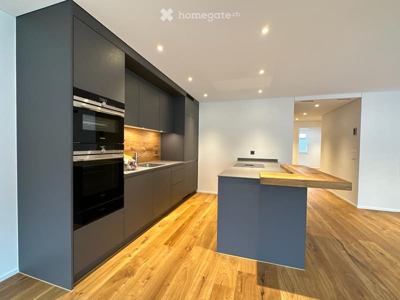 Modern kitchen with dark grey cabinets, wooden flooring, stainless steel oven, island with wooden countertop, and built-in lighting.
