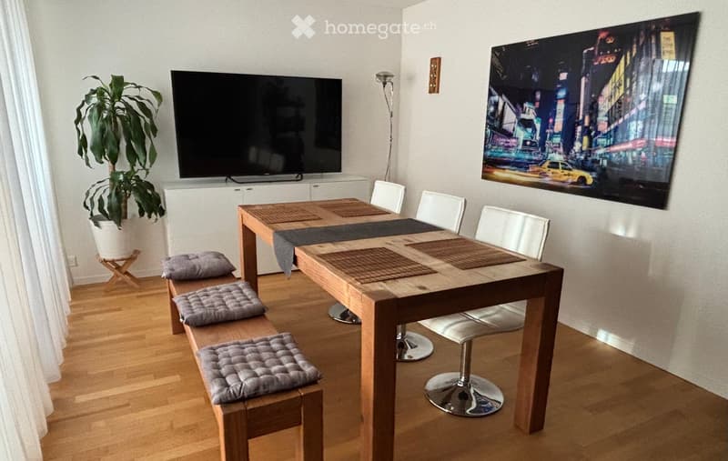 A modern living room with a wooden dining table, four white chairs, a bench with three grey cushions, a television, a potted plant, and a large cityscape picture on the wall.