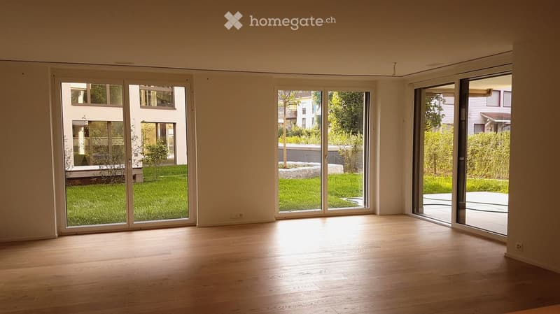 Bright, empty room with large sliding glass doors opening to a garden, wooden flooring, and white walls.