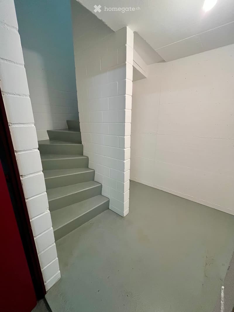 A narrow hallway with white brick walls, a green-painted staircase leading upwards, and a smooth green floor.