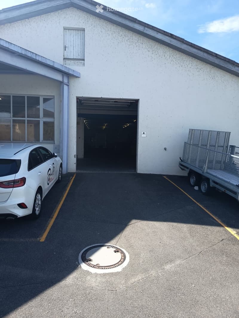 White building with a garage entrance, a parked car, and a trailer with a cage on the right side.