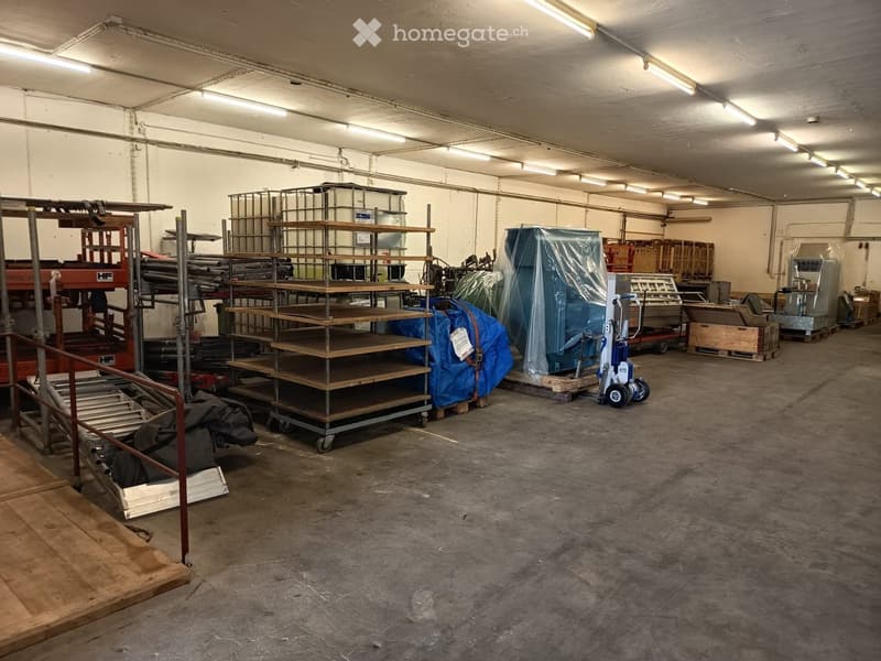 Large, empty warehouse space with concrete floors, white walls, and industrial shelving units. No furniture or equipment is present.