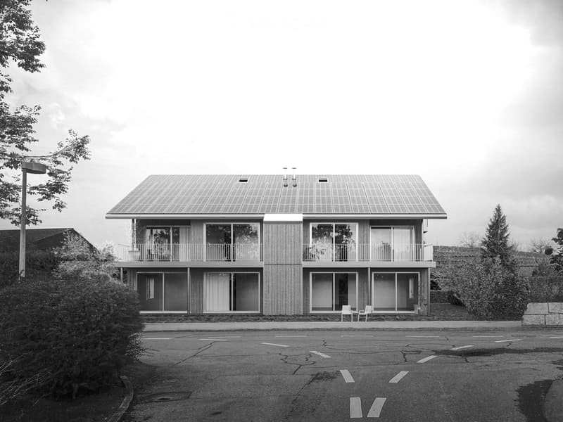 Two-story modern building with large windows, balconies, and a flat roof.