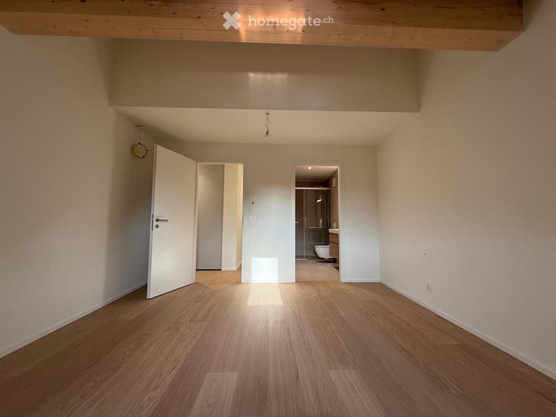 Empty room with wooden flooring, white walls, and open doors leading to other rooms.