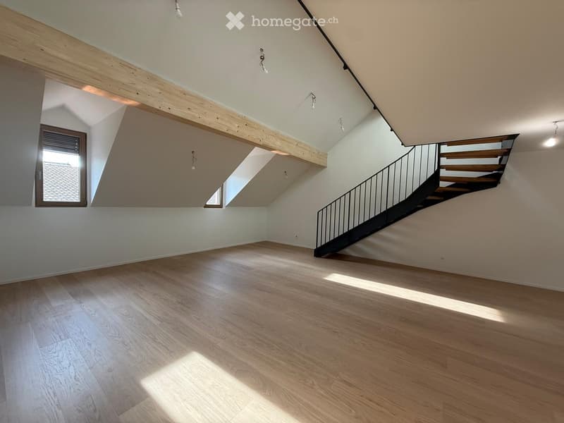 Empty room with wooden flooring, white walls, and a staircase leading upwards. Natural light streams in from a window on the left side.
