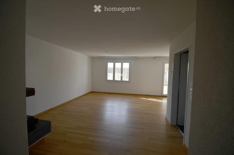 Empty room with wooden flooring, white walls, and a single window allowing natural light to enter. The space is completely unfurnished, showing only the basic structure of the room.