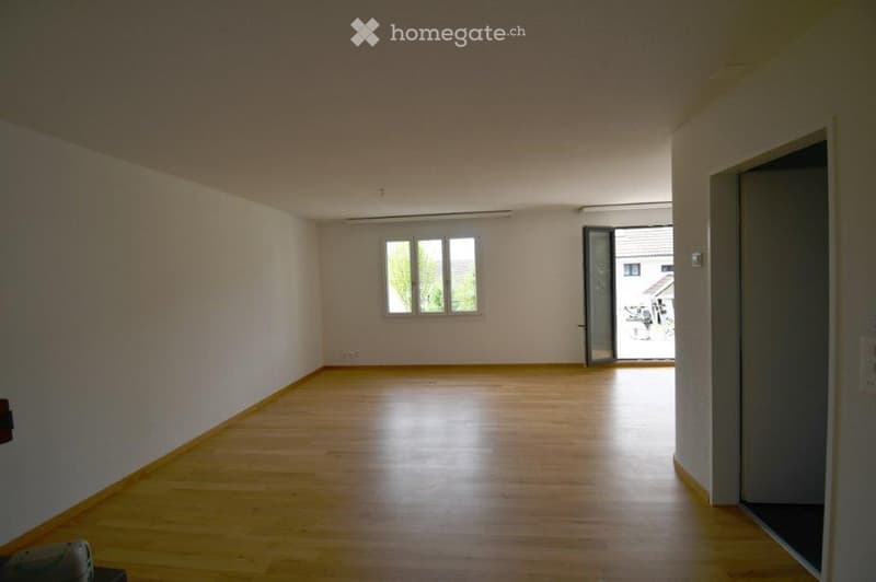 Empty room with wooden flooring, white walls, and a large window allowing natural light. No furniture or equipment is present.