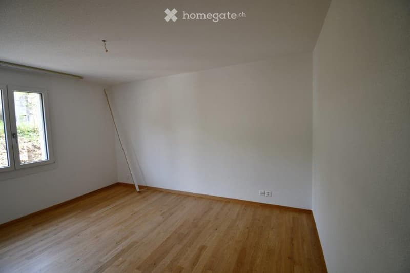 Empty room with wooden flooring, white walls, and a single window with a view of greenery outside. No furniture or equipment is present.