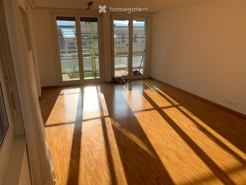 Empty room with wooden flooring, large glass sliding doors leading to a balcony, and natural light streaming in.