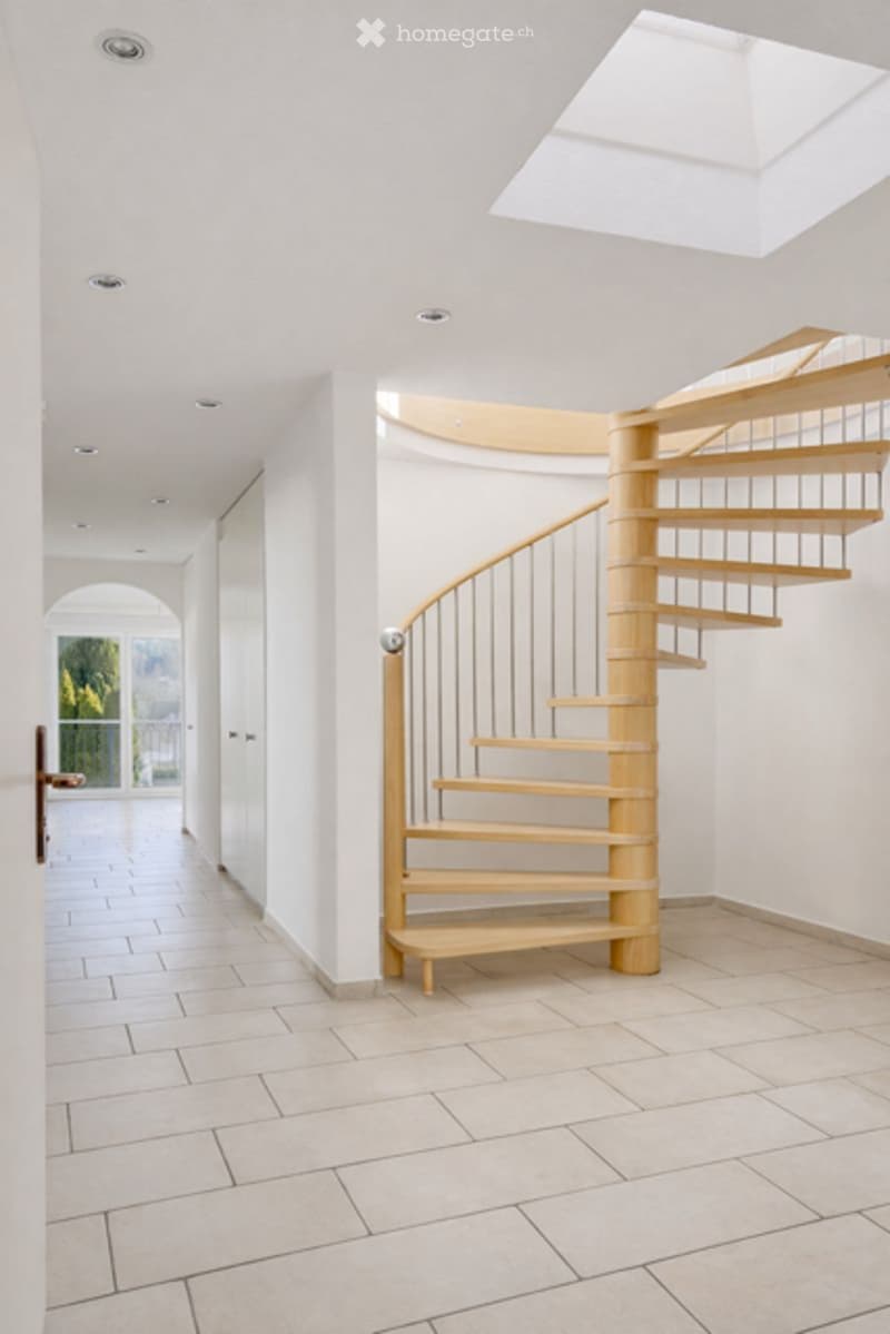 Modern hallway with a wooden spiral staircase, white walls, recessed lighting, and a skylight above.