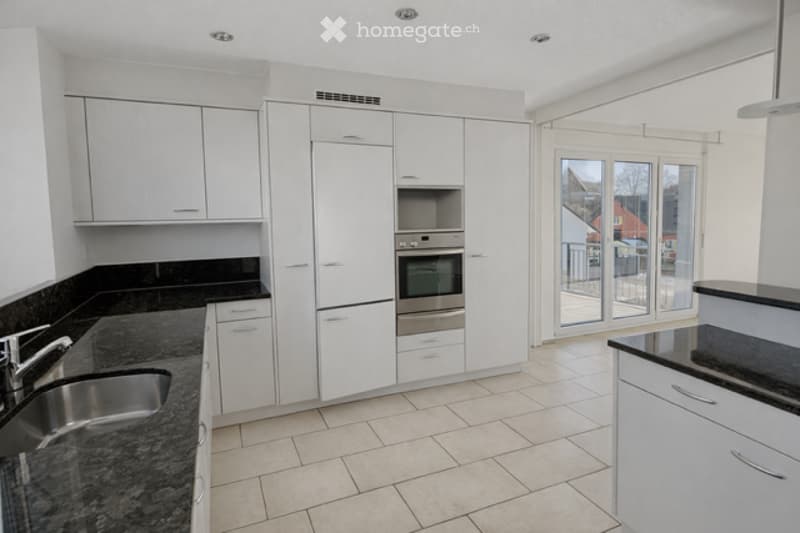 Modern kitchen with white cabinets, granite countertops, stainless steel sink, and built-in oven. Large sliding glass door leads to a balcony.