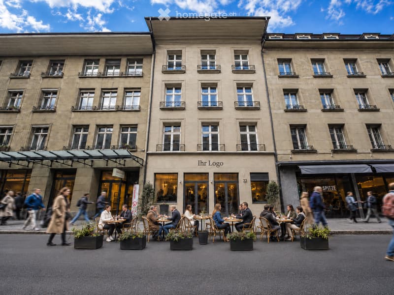 A multi-story building with large windows and balconies, featuring a restaurant with outdoor seating on the sidewalk.