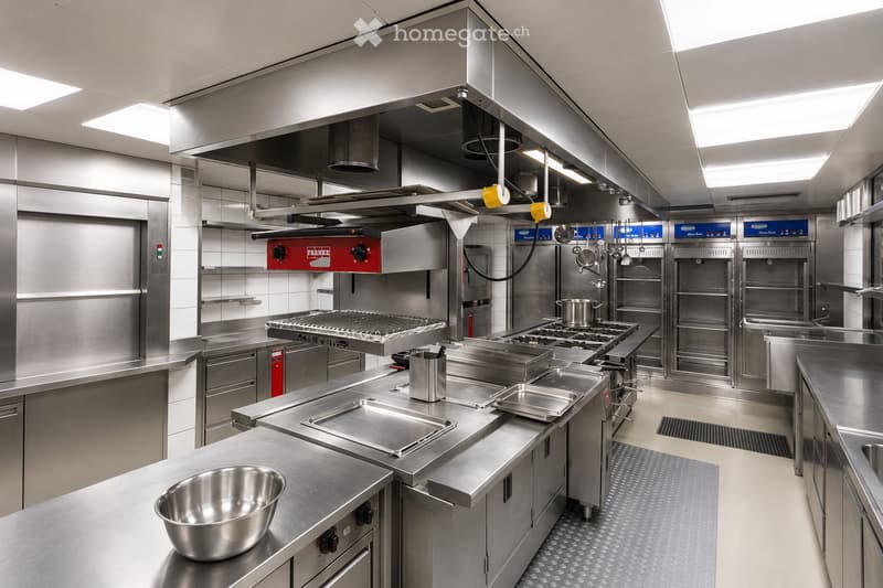 Commercial kitchen with stainless steel appliances, stove, oven, fryer, sink, and various cooking equipment.