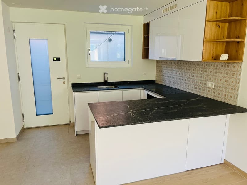 Modern kitchen with white cabinets, black countertops, and a sink. Features a window and a door leading outside.