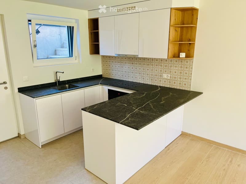 Modern kitchen with white cabinets, dark granite countertops, a sink, and a dishwasher. Features a wooden shelf and a window with a view.