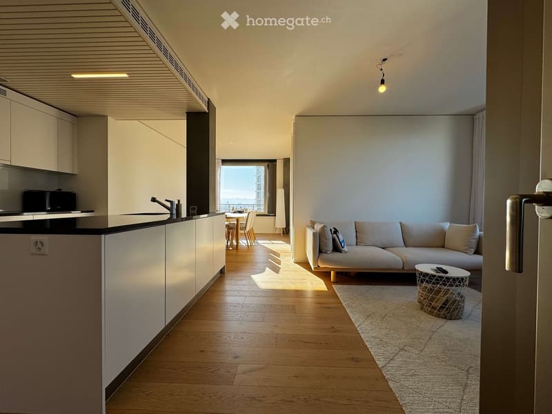 Open-plan living and dining area with a modern sofa, coffee table, and a small dining set. The kitchen features sleek cabinets and a sink.