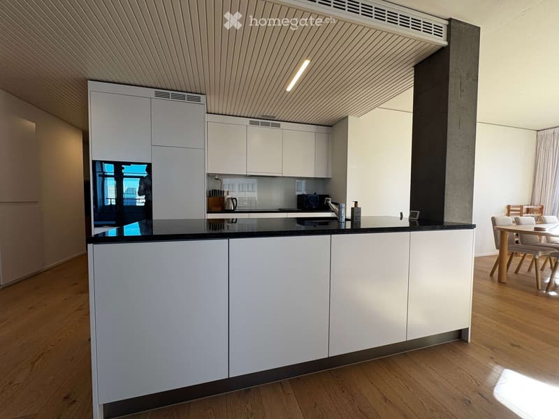 Modern kitchen with white cabinets, black countertop, and wooden flooring. Includes a dining area with a table and chairs.