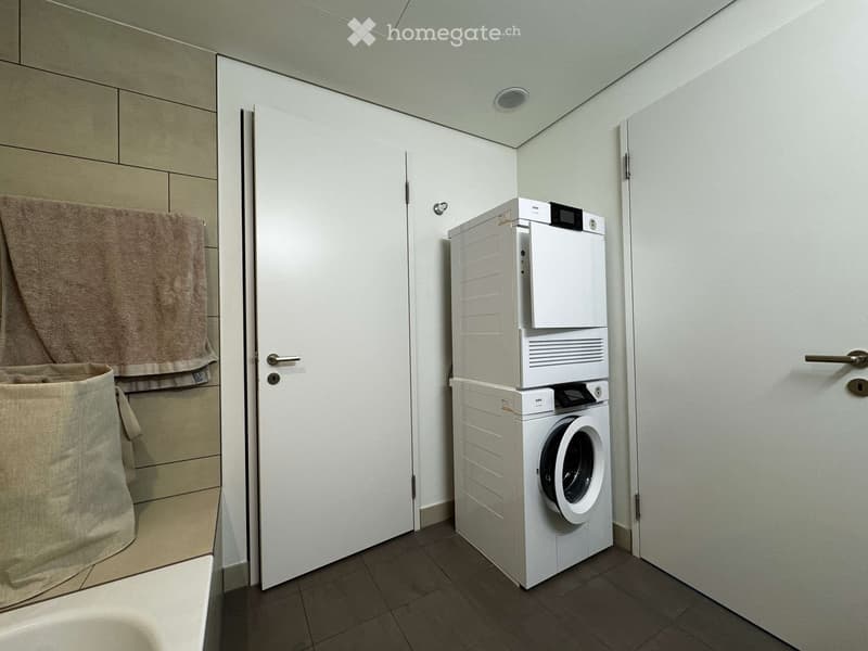 Compact laundry area with a stacked washing machine and dryer, a towel hanging on a rack, and a laundry basket.