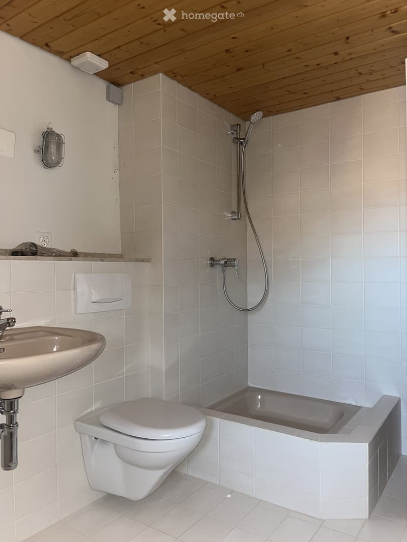 Modern bathroom with white tiled walls and floor, featuring a toilet, bathtub, sink, and showerhead.