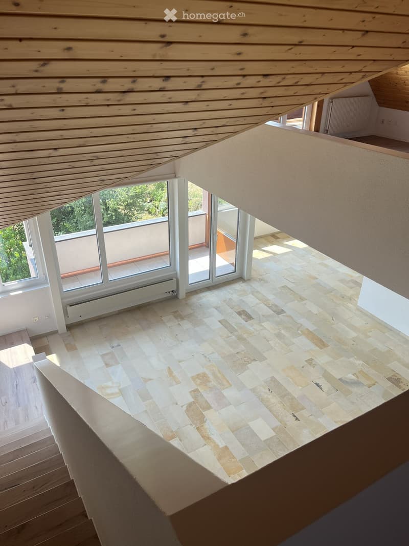 An empty room with a wooden ceiling, tiled floor, and large windows leading to a balcony. The space is unfurnished and appears to be part of a modern interior design.