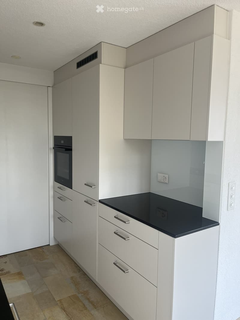 Modern kitchen with white cabinets, a black countertop, and a built-in oven. The floor is tiled in a warm, earthy tone.
