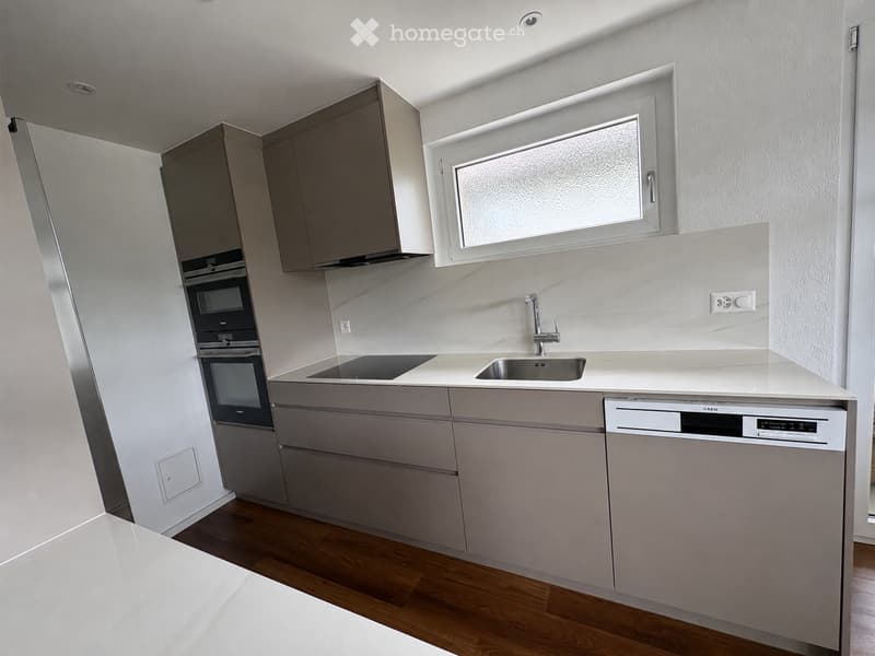 Modern kitchen with light grey cabinets, a sink, a dishwasher, and an oven. The countertop is white, and the floor is wooden.