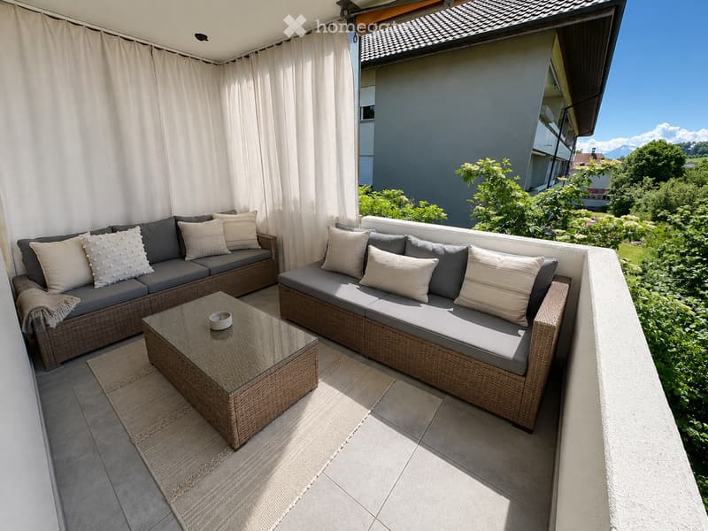 Balcony with two wicker sofas, cushions, coffee table, and curtains.