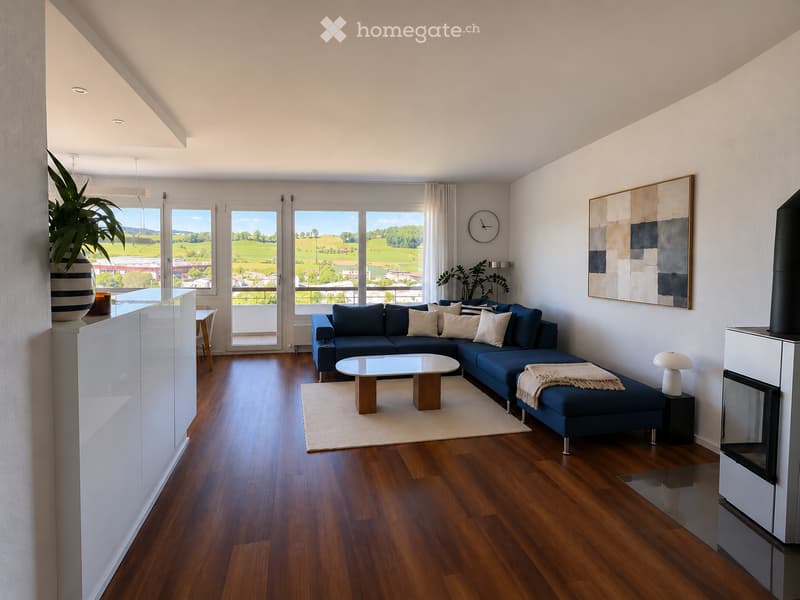 Modern living room with wooden flooring, large windows offering a scenic view, a blue sectional sofa, a glass coffee table, a small dining table with chairs, a lamp, a clock, a painting, and a fireplace.