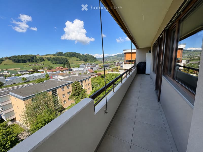 Balcony with tiled floor, metal railing, and scenic view of a town and surrounding hills.