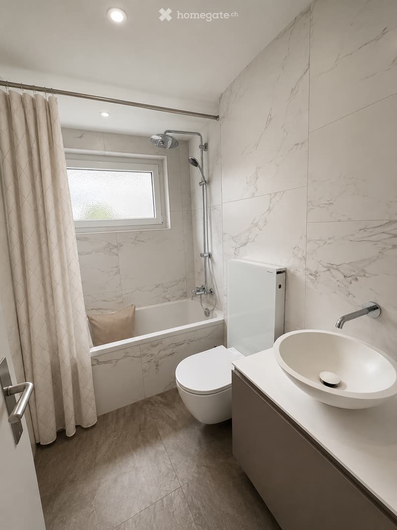 Modern bathroom with marble tiles, a bathtub, toilet, sink, and a shower area with a curtain.
