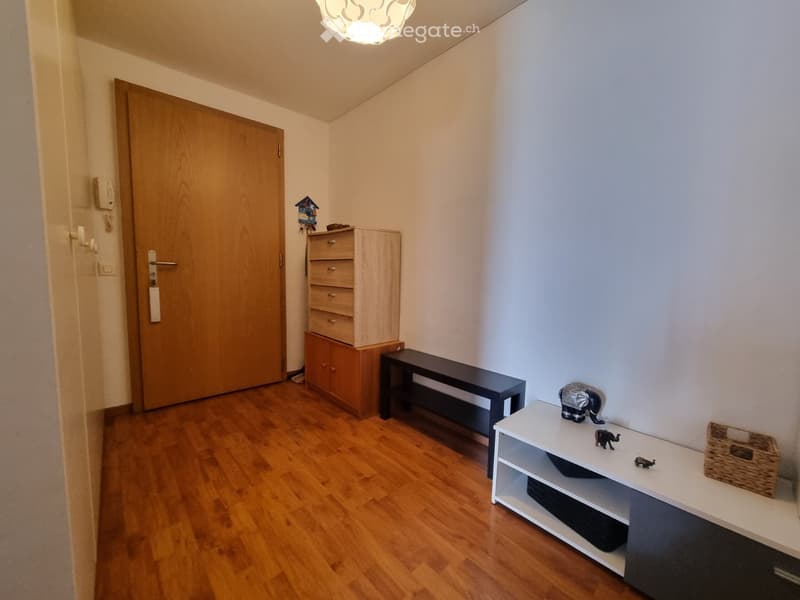 A small hallway with wooden flooring, a bench, a shelf with decorative items, a drawer unit, and a small table with a statue and basket.