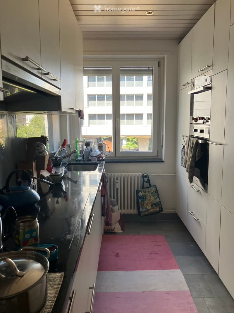 Modern kitchen with white cabinets, stainless steel appliances, a window with a city view, and various kitchen items on the counter.