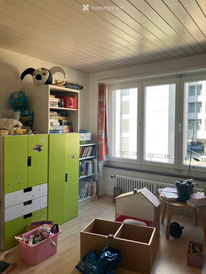 A child's room with a green wardrobe, a bookshelf, a small wooden stool, a toy house, a globe, and various toys and storage boxes.