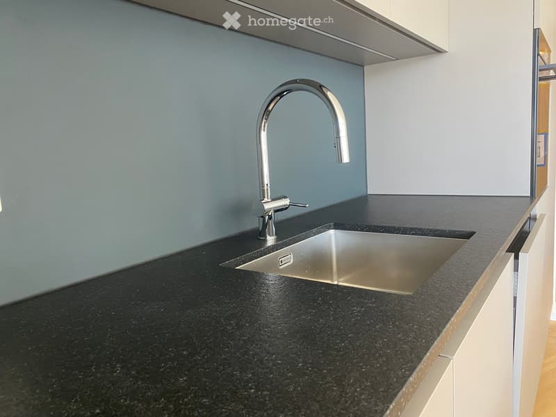 Modern kitchen with a black granite countertop, stainless steel sink, and sleek faucet.