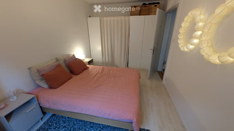 Cozy bedroom with a double bed, pink bedding, nightstand, mirror, and wicker baskets on top of the wardrobe.