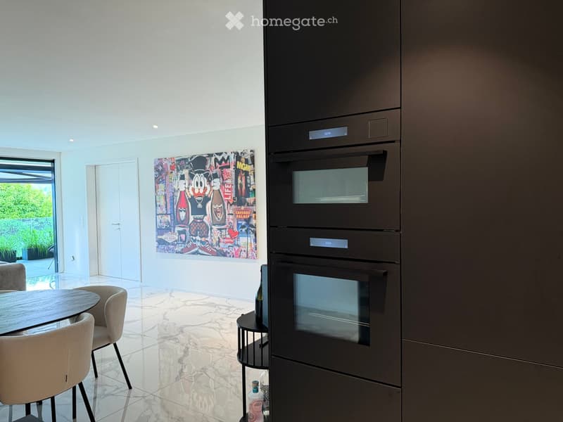 Modern kitchen with built-in ovens, a round dining table with chairs, and a colorful artwork on the wall.