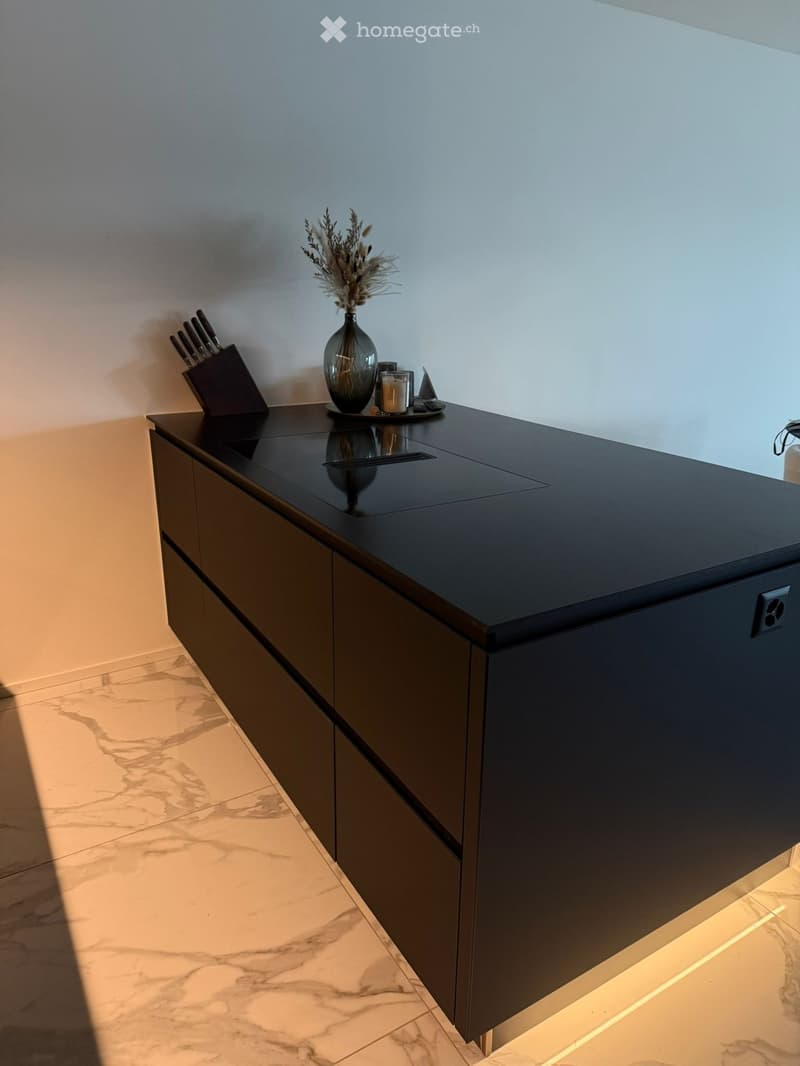 Modern kitchen with dark countertops, built-in cabinets, and a sleek design. Includes a knife block, vase with dried flowers, and a candle on the counter.