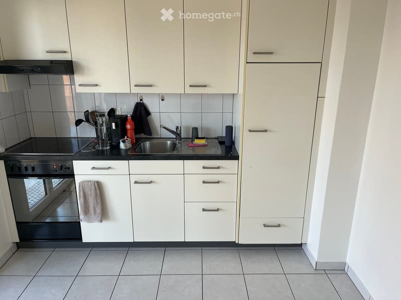 Modern kitchen with white cabinets, stainless steel oven, sink, and various small appliances and utensils on the counter.