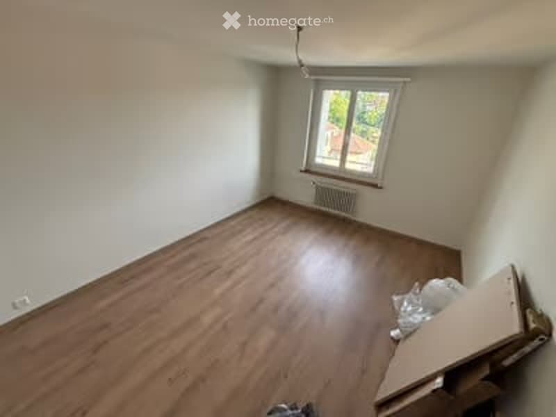 Empty room with wooden flooring, white walls, and a single window with a radiator below it. No furniture or equipment is present.