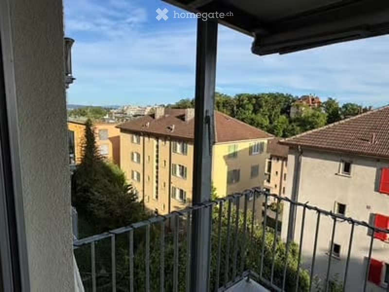 Balcony overlooking a cityscape with multiple residential buildings, trees, and a clear blue sky.