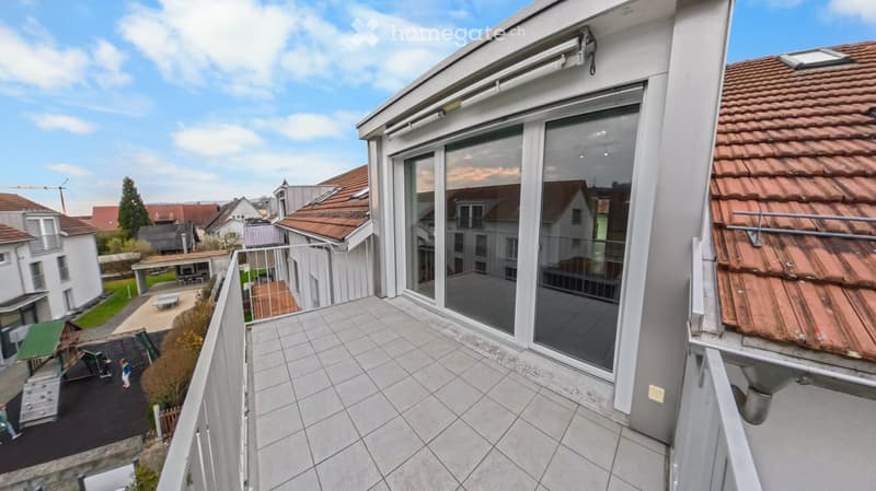 Balcony with tiled floor, large glass sliding doors, metal railing, overlooking a residential area with houses and a playground.