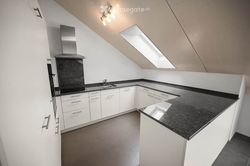 Modern kitchen with white cabinets, black granite countertops, stainless steel range hood, and built-in sink under natural light from skylights.