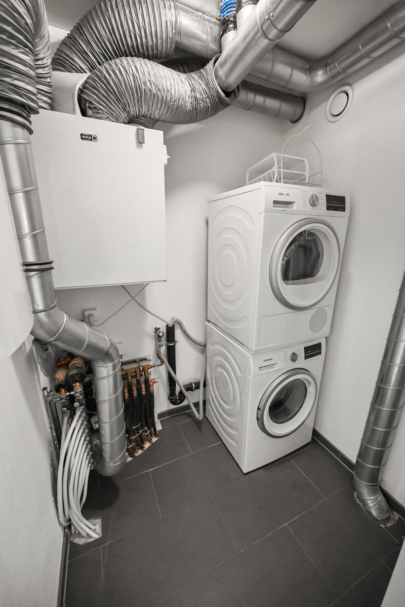 Modern bathroom with a washing machine and dishwasher, visible plumbing and heating system.