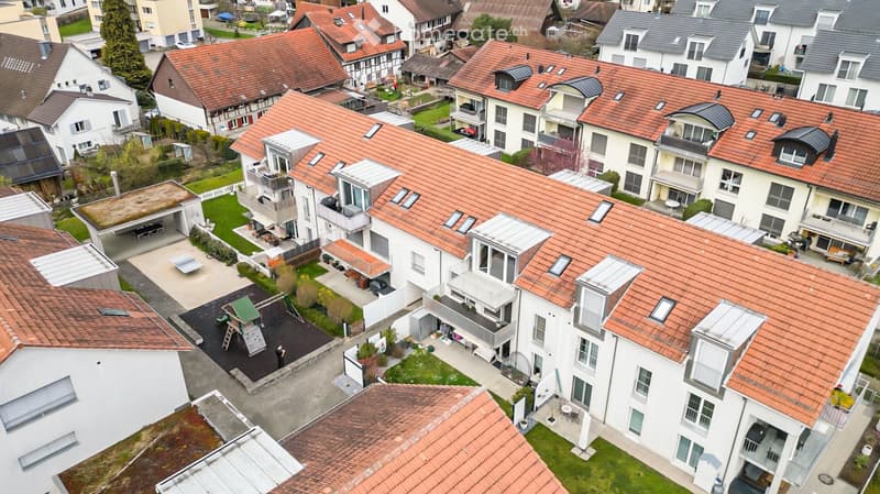 Aerial view of a residential complex with multiple buildings, red-tiled roofs, balconies, and green spaces.