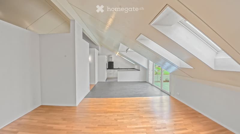 Bright, open loft-style room with wooden flooring, white walls, and skylights. Features a modern kitchen area with white cabinets, a refrigerator, and a kitchen island.
