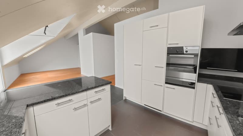 Modern kitchen with white cabinets, granite countertops, and stainless steel oven. Wooden flooring in part of the space.