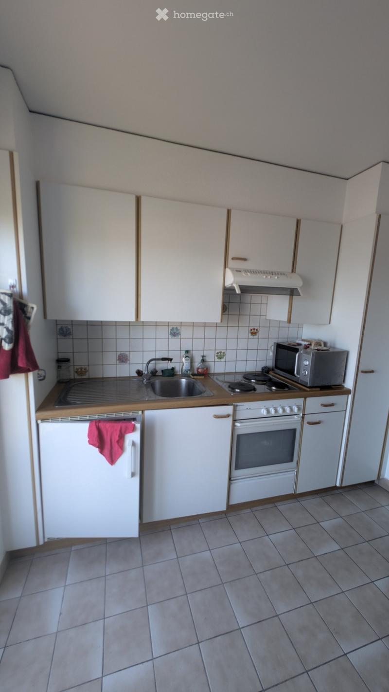 Compact kitchen with white cabinets, a sink, stove, microwave, and refrigerator. The countertops are wooden, and the floor is tiled.