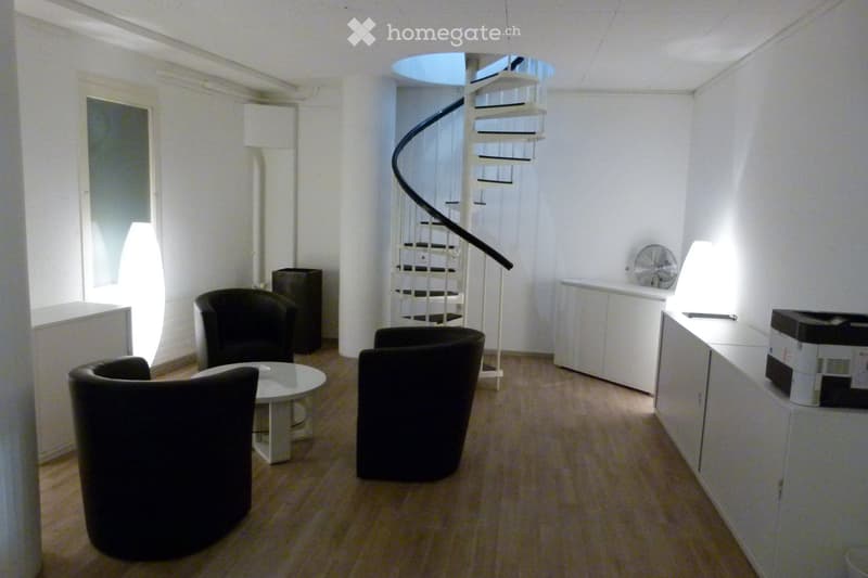 Modern, minimalist room with a spiral staircase, several black chairs, a round white table, a fan, and a white cabinet with a printer on top.