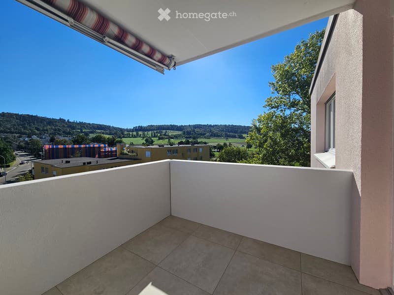 Balcony with tiled floor, white railing, and retractable awning, overlooking a scenic landscape with trees and hills.