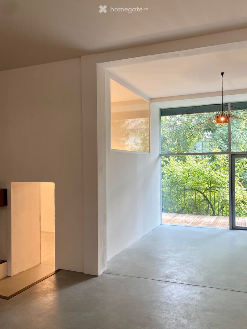 Empty room with large windows and a view of greenery, featuring a modern, minimalist design with concrete floors and white walls.